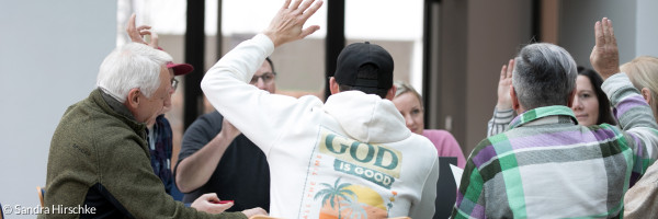 Einige Menschen sitzen am Tisch und heben die Hand bei einer Abstimmung