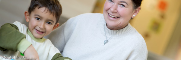 Eine Erzieherin hilft einem Kind beim Gemüseschneiden