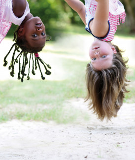 Zwei Mädchen hängen kopfüber an einer Schaukel